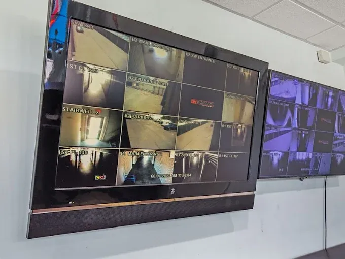 Two wall-mounted security monitors displaying multiple camera feeds of hallways, entrances, and parking areas