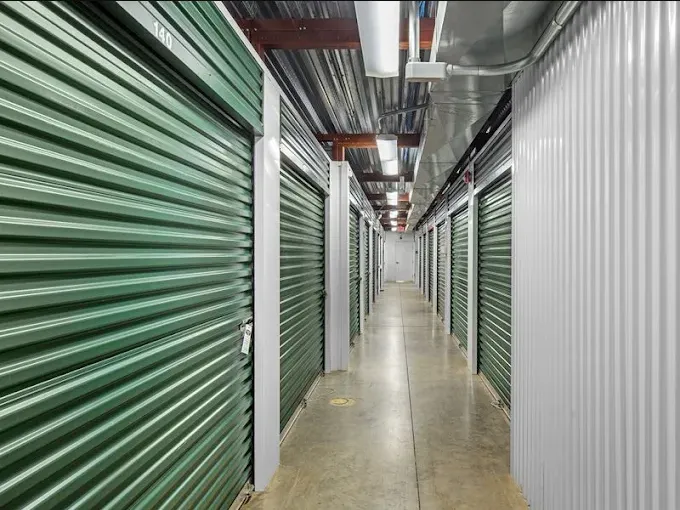 Indoor climate-controlled storage units with green roll-up unit doors and white metal siding under bright overhead lighting