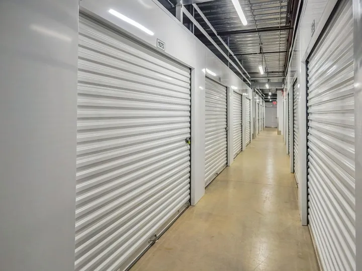 A well-lit hallway with indoor climate-controlled storage in Augusta on Cooper Dr, featuring rows of white corrugated metal roll-up doors with unit numbers
