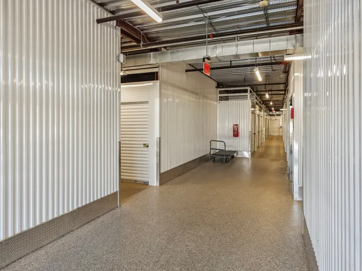 A white roll-up Climate-controlled storage unit in Augusta on Cooper Dr, next to a metal push cart in a brightly lit hallway
