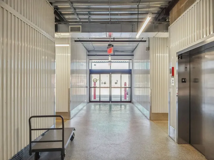 Bright indoor storage hallway with white corrugated walls, an elevator, a push cart, and glass exit doors at Storage Star Self-Storage in Augusta on Cooper Dr