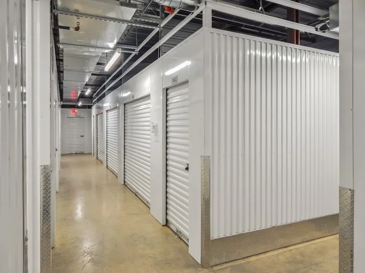 Hallway of indoor climate-controlled storage in Augusta on Cooper Dr, featuring white corrugated metal units with roll-up doors and diamond plate corner guards