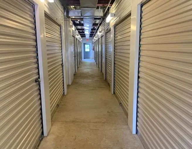Indoor hallway lined with rows of climate-controlled storage units in Glassboro, NJ, with beige corrugated metal roll-up doors and overhead lighting