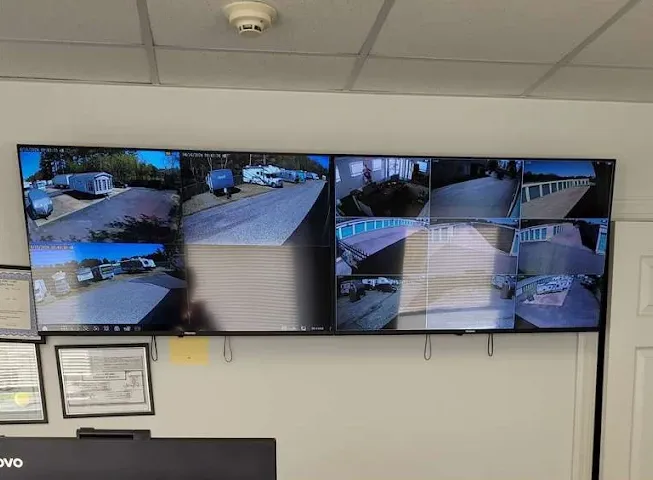 Two wall-mounted television monitors displaying multiple security camera feeds of the Glassboro Storage Star storage facility and vehicle parking lot