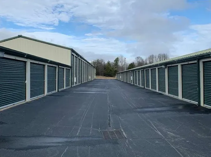 Paved driveway between two rows of outdoor self-storage buildings with dark green roll-up doors