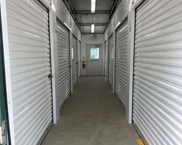 Indoor Winston-Salem storage facility hallway featuring two rows of white corrugated roll-up doors and a distant exit sign