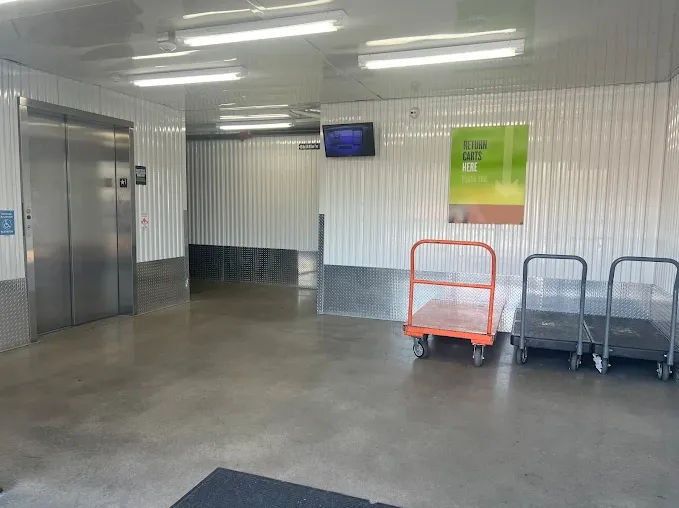 Indoor storage facility loading area with a freight elevator, overhead lighting, and several flatbed moving carts