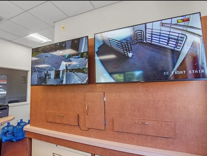 Two television monitors mounted on a wall displaying real-time security camera footage of facility grounds and stairs