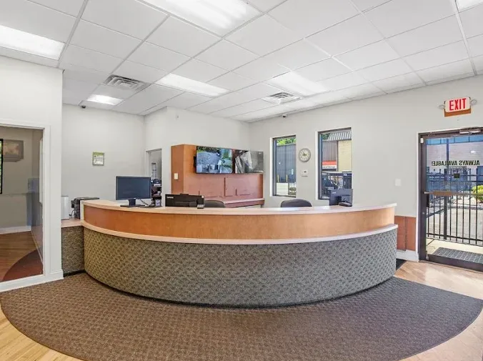 A curved reception desk in a brightly lit storage facility office with security monitor screens and windows