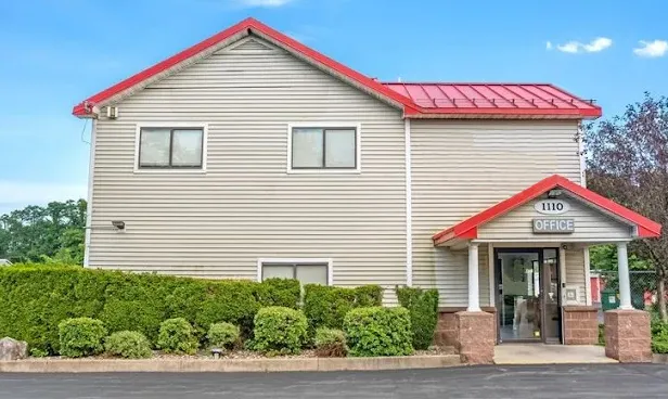 Two-story tan siding office building at Storage Star Self-Storage in Schenectady, with a red roof, front entrance, and green hedge landscaping