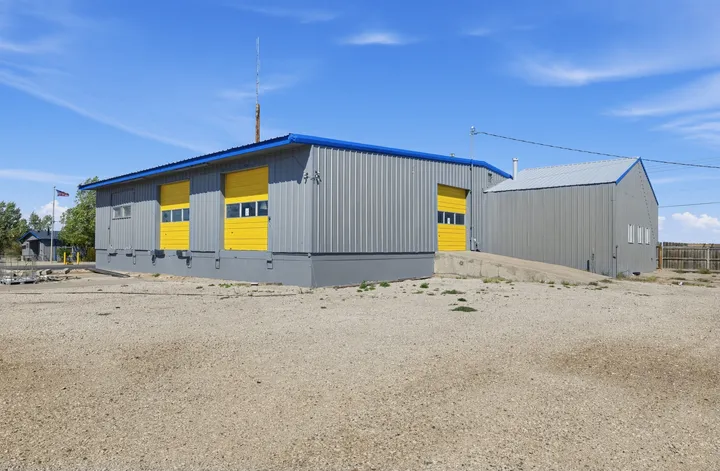 Grey metal warehouse storage building in Laramie on Skyline Rd with yellow roll-up doors and a concrete loading ramp under a blue sky
