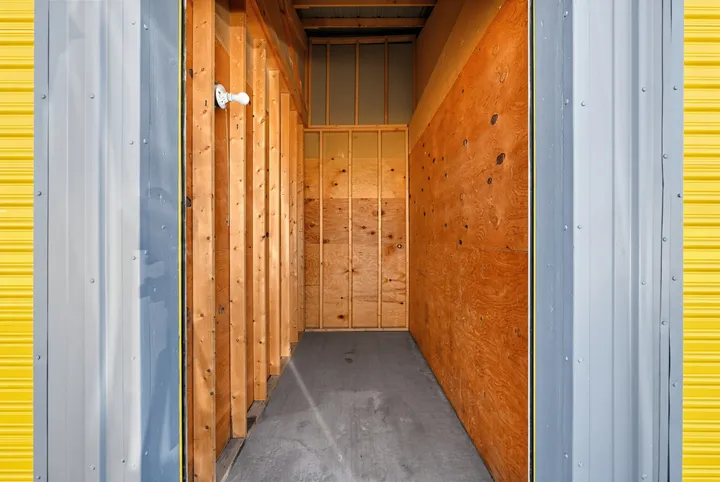 An empty 5x10 storage unit in Laramie on Skyline Rd, featuring wood stud walls, plywood paneling, and a single light bulb