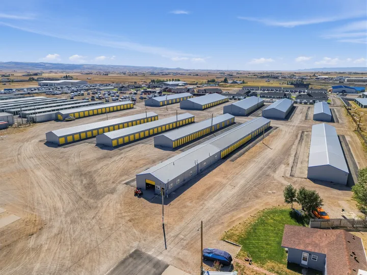 Aerial view of multiple drive-up storage buildings in Laramie on Skyline Rd with yellow roll-up doors and gravel driveways under blue sky