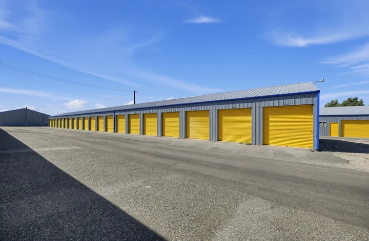 Row of gray drive-up storage units in Laramie, WY, with yellow roll-up doors along a paved driveway under a blue sky