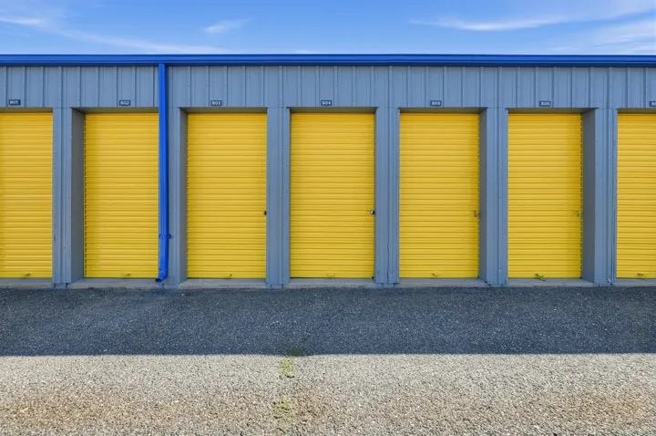 A row of yellow drive-up storage units in Laramie on Skyline Rd with gray siding and blue trim along a paved driveway