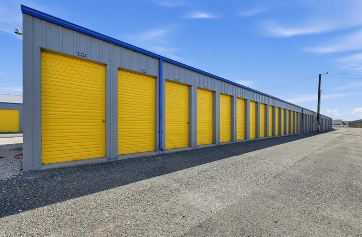 Row of gray drive-up storage units in Laramie on Skyline Rd, with yellow roll-up doors along a paved driveway under a blue sky