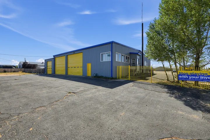 A gray warehouse storage building in Laramie, WY, with yellow roll-up doors, a yellow fence, and a paved lot