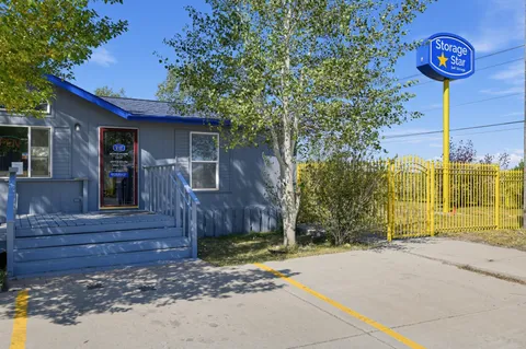 Gray office at Storage Star Self-Storage in Laramie on Skyline Rd with blue trim, porch stairs, and a yellow metal gate next to a tall pylon sign