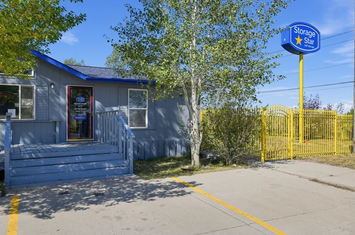 Gray office at Storage Star Self-Storage in Laramie on Skyline Rd with blue trim, porch stairs, and a yellow metal gate next to a tall pylon sign