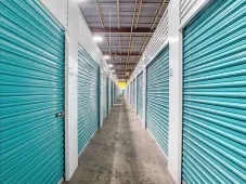 Bright blue roll-up doors line a long, well-lit indoor storage hallway with white walls and high ceilings
