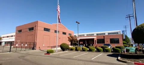 Exterior view of a red brick storage facility with a flagpole and paved parking lot