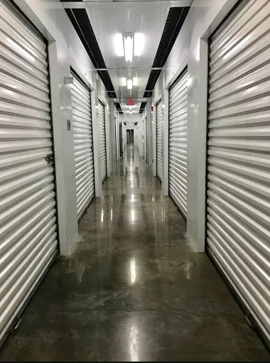 Indoor storage hallway with polished concrete floors and white roll-up metal doors under bright ceiling lights