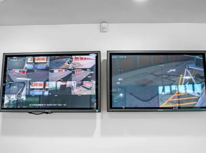 Two wall-mounted security monitors displaying live video feeds of storage unit driveways and hallways