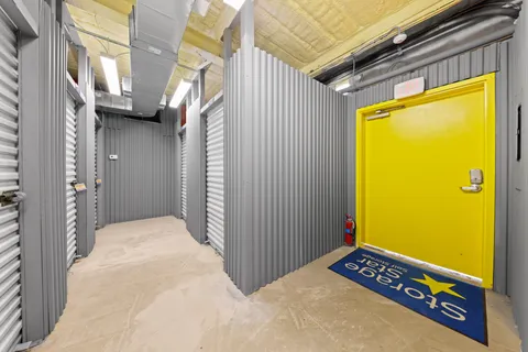 Interior storage hallway with climate-controlled storage units, graroll-up doors, a bright yellow exit door, and Storage Star welcome mat