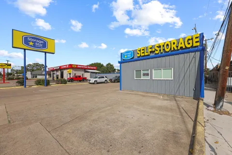 Gray office at Storage Star self-storage in Irving, TX, on N O'Connor Rd with a yellow sign, paved lot, and parked vehicles under a blue sky