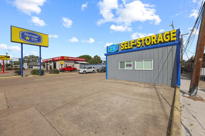 Gray office at Storage Star self-storage in Irving, TX, on N O'Connor Rd with a yellow sign, paved lot, and parked vehicles under a blue sky