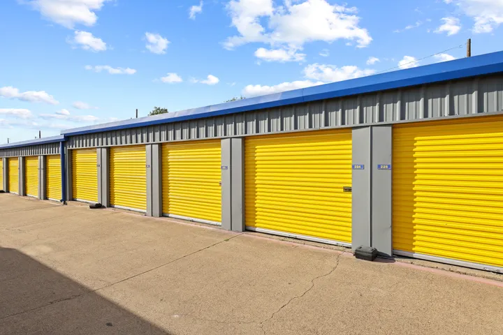 A row of outdoor drive-up storage units in Irving, TX, at Storage Star on N O'Connor Rd with yellow roll-up doors and blue roof trim