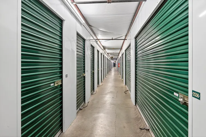 A hallway featuring rows of climate-controlled storage units in Vacaville, with green roll-up doors and white corrugated walls