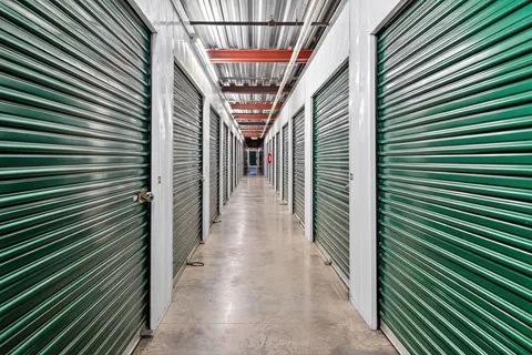 Brightly lit interior hallway featuring rows of climate-controlled storage units in Vacaville on Bella Vista Rd, with green metal roll-up doors and concrete flooring