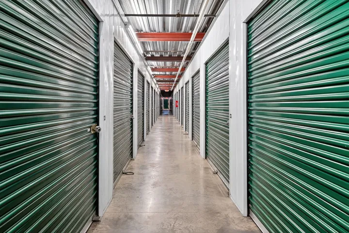 Brightly lit interior hallway featuring rows of climate-controlled storage units in Vacaville on Bella Vista Rd, with green metal roll-up doors and concrete flooring