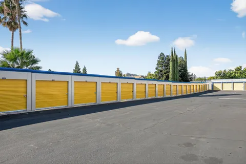 A row of drive-up storage units in Vacaville, CA, with yellow roll-up doors and a paved asphalt driveway