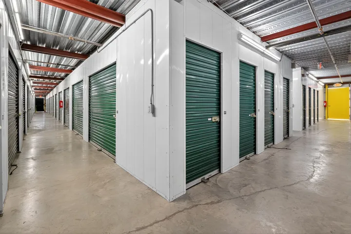 Indoor climate-controlled storage units in Vacaville, CA, with white metal walls, green roll-up doors, and concrete flooring under bright lights