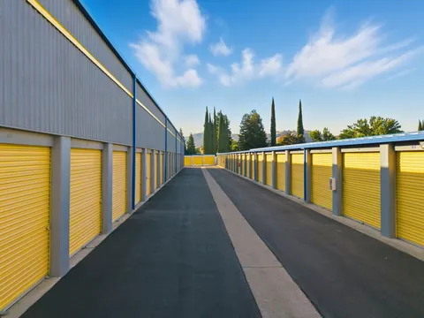 Outdoor drive-up storage units in Vacaville on Bella Vista Rd with yellow roll-up doors and asphalt drive aisles under a blue sky