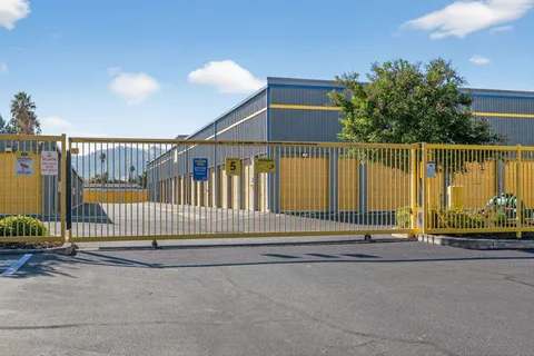 A yellow access gate in front of gray multi-story self-storage buildings with yellow drive-up units in Vacaville on Bella Vista Rd