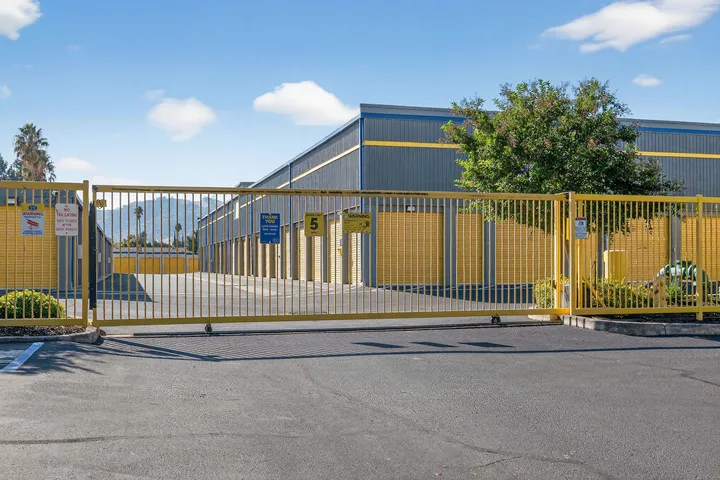A yellow access gate in front of gray multi-story self-storage buildings with yellow drive-up units in Vacaville on Bella Vista Rd