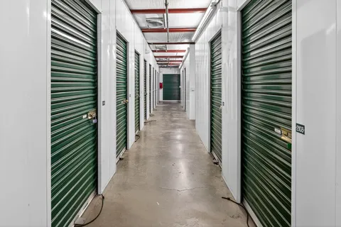 Indoor hallway with white walls, concrete floors, and rows of green climate-controlled storage units in Vacaville, CA, on Bella Vista Rd