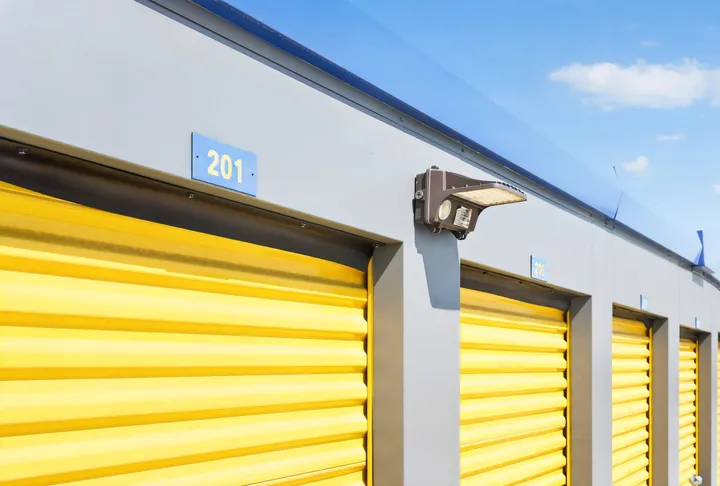 Close-up of drive-up storage units in Cheyenne at Wyott Dr, with yellow roll-up storage unit doors, a security light, and unit number signage