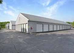 A row of outdoors grey self-storage buildings in York, ME, featuring white drive-up unit doors and asphalt driveways