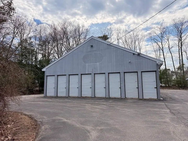A row of white roll-up doors on a grey gabled storage building with an asphalt driveway
