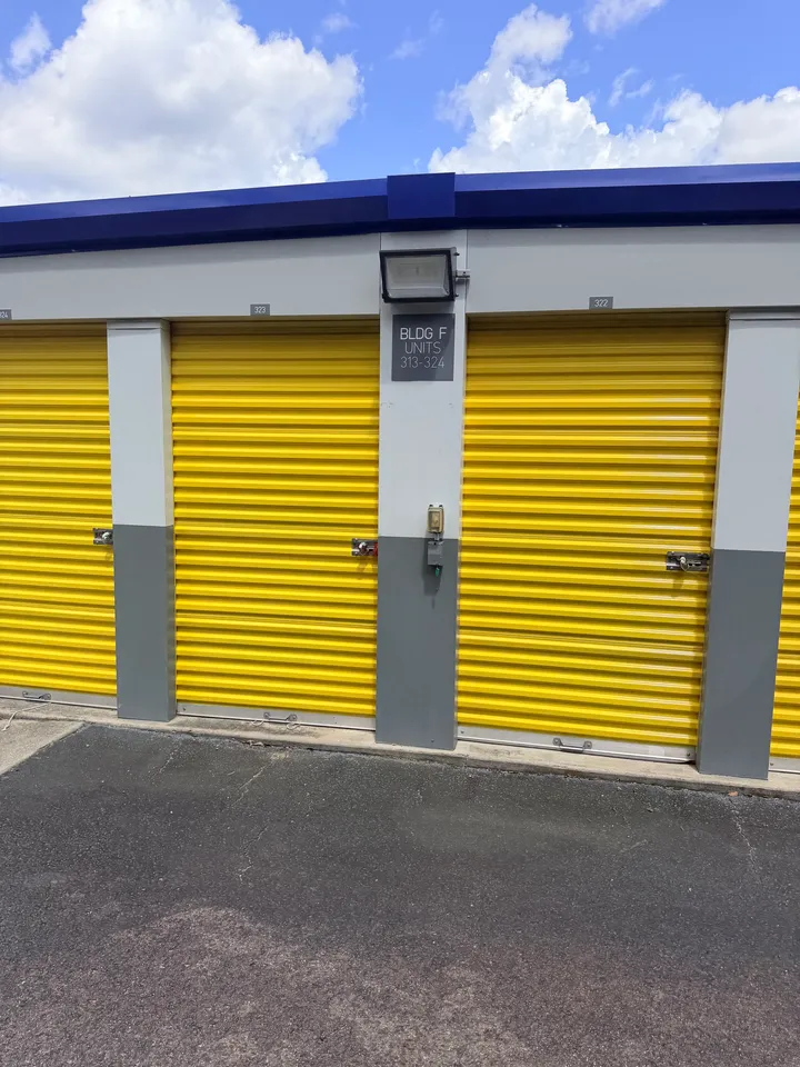 Exterior drive-up storage units in Aiken, SC, with yellow roll-up doors, a security light, and building signage