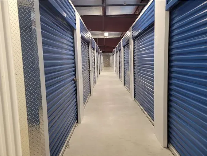 Indoor storage facility hallway with blue roll-up doors and white metal trim along a concrete floor