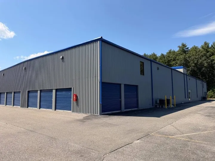 Gray corrugated metal building featuring warehouse storage in Coventry, RI, with several blue roll-up doors and a paved drive-up area