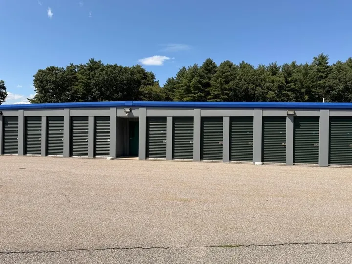 A row of drive-up storage units in Coventry, RI, with green roll-up doors and a blue roof trim