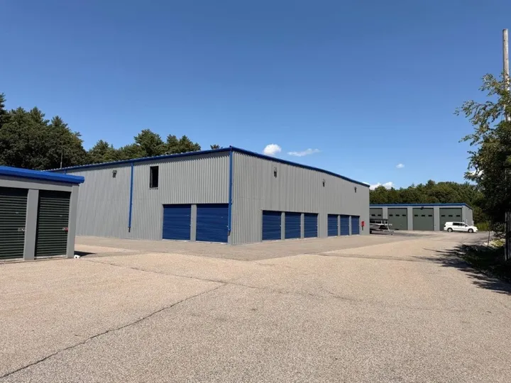Large gray buildings featuring drive-up storage units in Coventry on 1185 Tigure Ave and a wide paved driving area under a blue sky