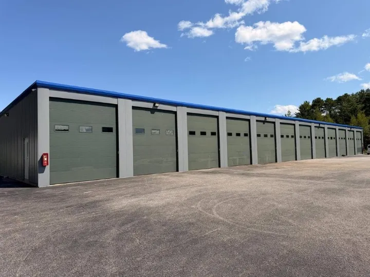 Row of outdoor drive-up workshop units in Coventry, RI, with green doors and windows along a wide asphalt drive aisle