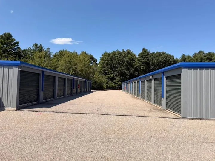 Two rows of outdoor drive-up storage units in Coventry, RI, with blue trim and green roll-up doors under a clear sky